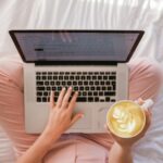 person using MacBook Pro and holding cappuccino